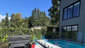 Ein modernes Haus mit Pool, überdachter Terrasse und gepflegtem Rasen.