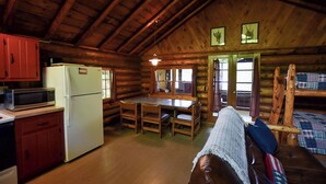 A log cabin interior with a kitchen, dining area, and a cozy seating area. - Cozy Adirondack Cabin-Lakeside Resort Camp 1 (Olmstedville)