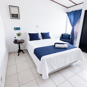 A hotel room with a bed, a small table with a plant, a chair, and a window with curtains.