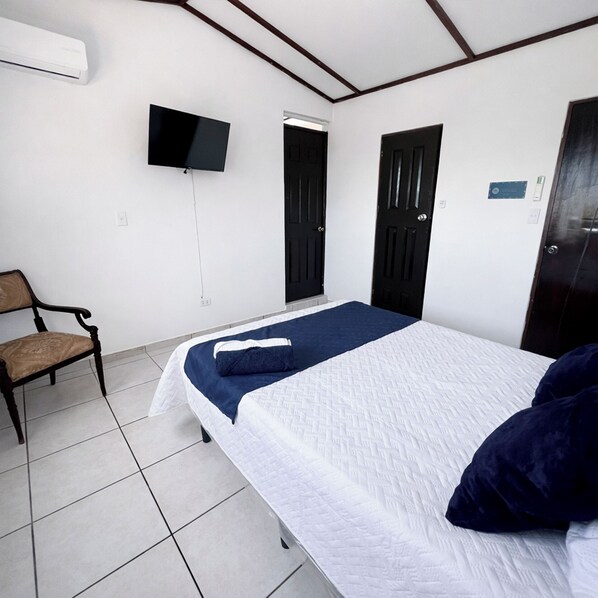 A hotel room with a bed, a chair, a TV, and two doors. - Gioventu  (San Salvador)