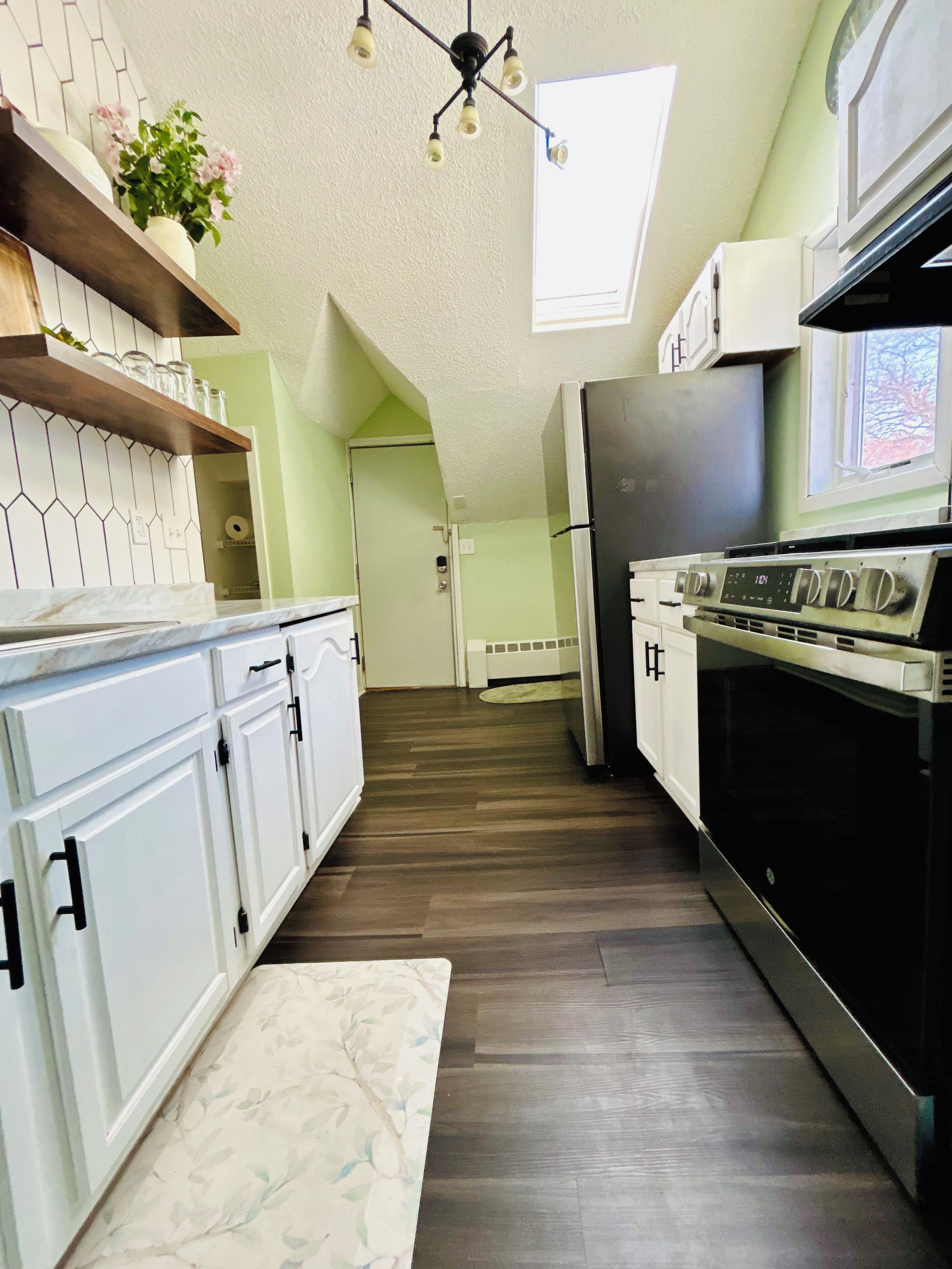 A kitchen with white cabinets, a black refrigerator, and a wooden floor.