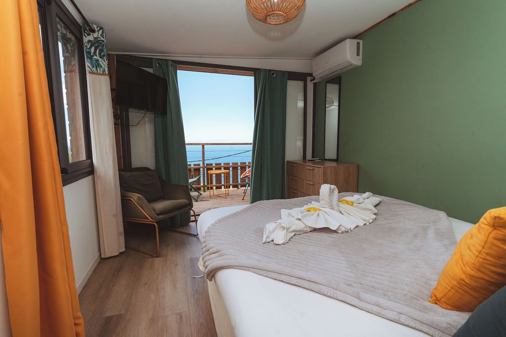 Et hotelværelse med seng, stol, lille bord, balkon med udsigt og en aircondition.