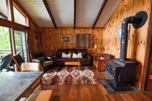 Ein gemütliches Blockhauss-Interieur mit Holzausstattung, einer Couch, einem Tisch, einem Kamin und einem Fenster mit Vorhängen.
