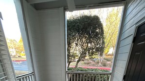 Eine überdachte Veranda mit zwei Metallstühlen, einem Betonboden und Blick auf einen Baum und einen roten Zaun.