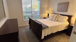 Ein Schlafzimmer mit Bett, Schreibtisch, Fenster mit Jalousien, Deckenventilator und Wandlampe.