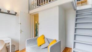 Et værelse med en grå sofa, et hvidt skrivebord, en trappe og en dør til et andet rum.
