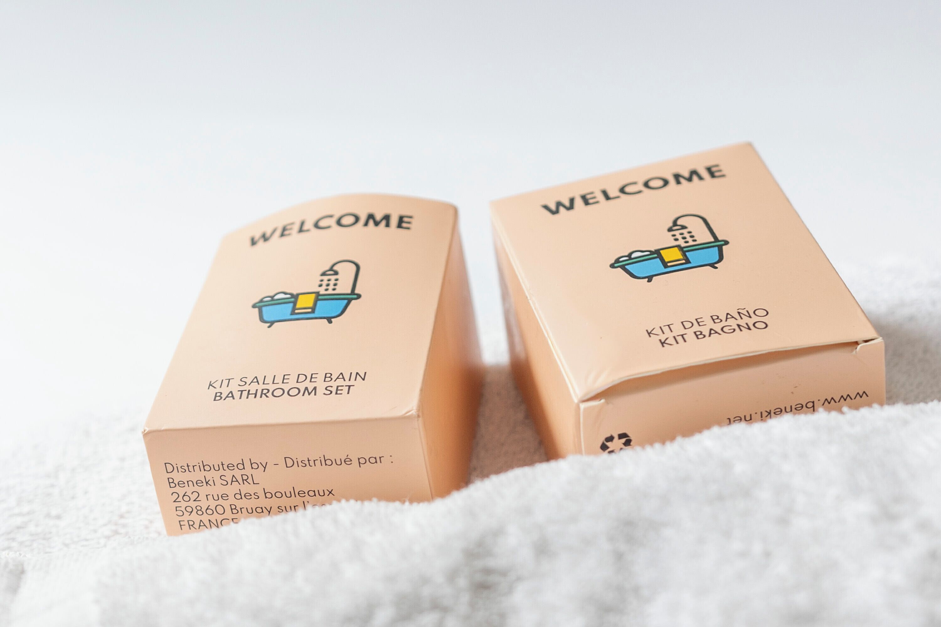 Twee kartonnen dozen, gelabeld 'Welcome' en 'Kit de Bain', met een illustratie van een badkamer set.