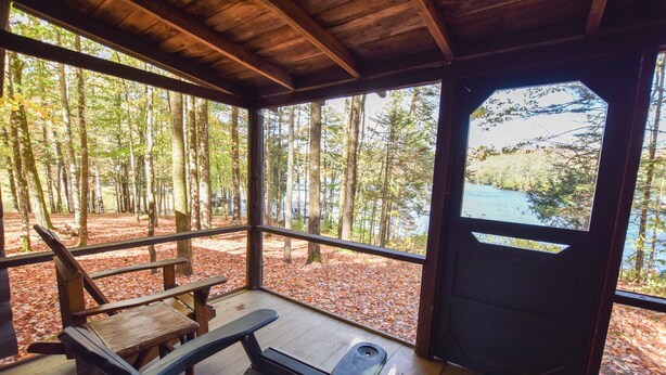 A covered outdoor seating area with benches and a table, surrounded by trees and a view of a lake. - Cozy Adirondack Cabin-Lakeside Resort Camp 3 (Olmstedville)