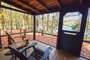 A covered outdoor seating area with benches and a table, surrounded by trees and a view of a lake. - Cozy Adirondack Cabin-Lakeside Resort Camp 3 (Olmstedville)
