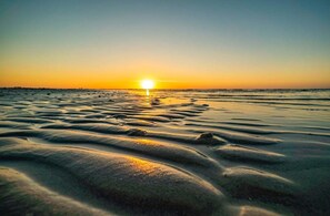 Uma praia com ondas suaves e um pôr do sol ao longe.