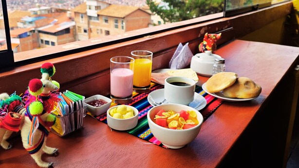 A breakfast table with food and drinks, a small toy, and a window view of a cityscape. - Mirador All Sur Cusco (Cusco)
