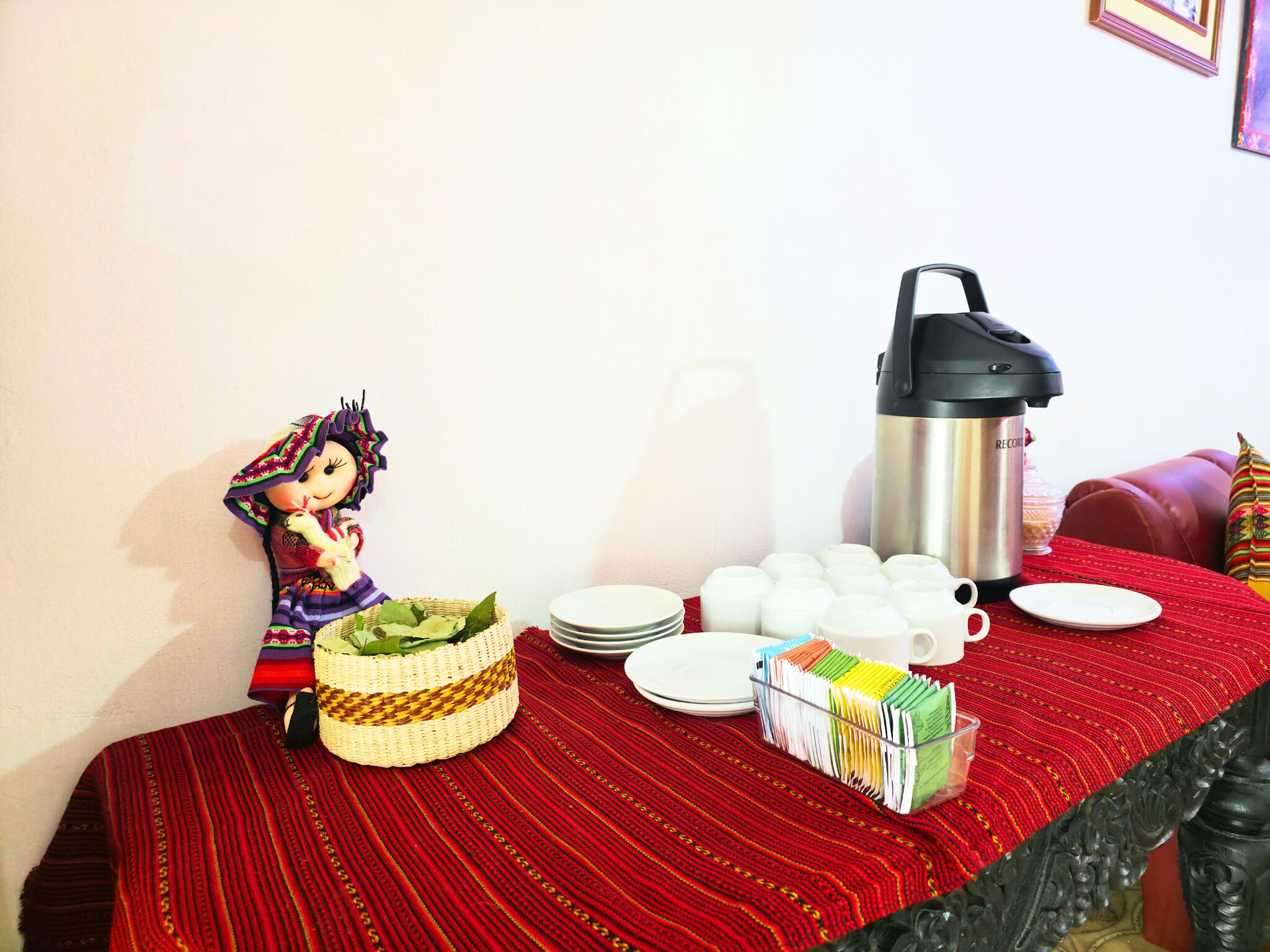 A dining table with a red tablecloth, a woven basket, a thermos, plates, and a decorative doll.