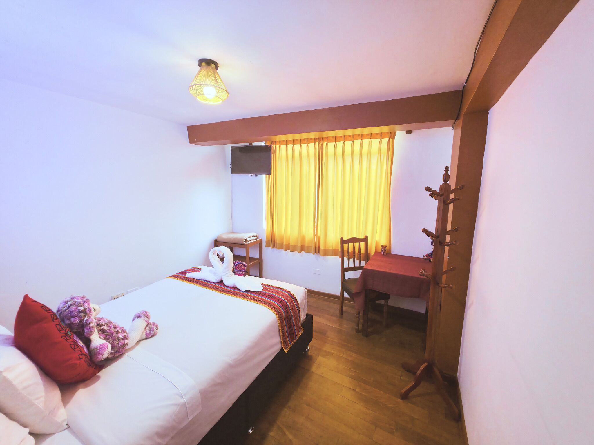Una habitación de hotel con cama, una silla, una mesa, una ventana con cortinas y una lámpara en el techo.