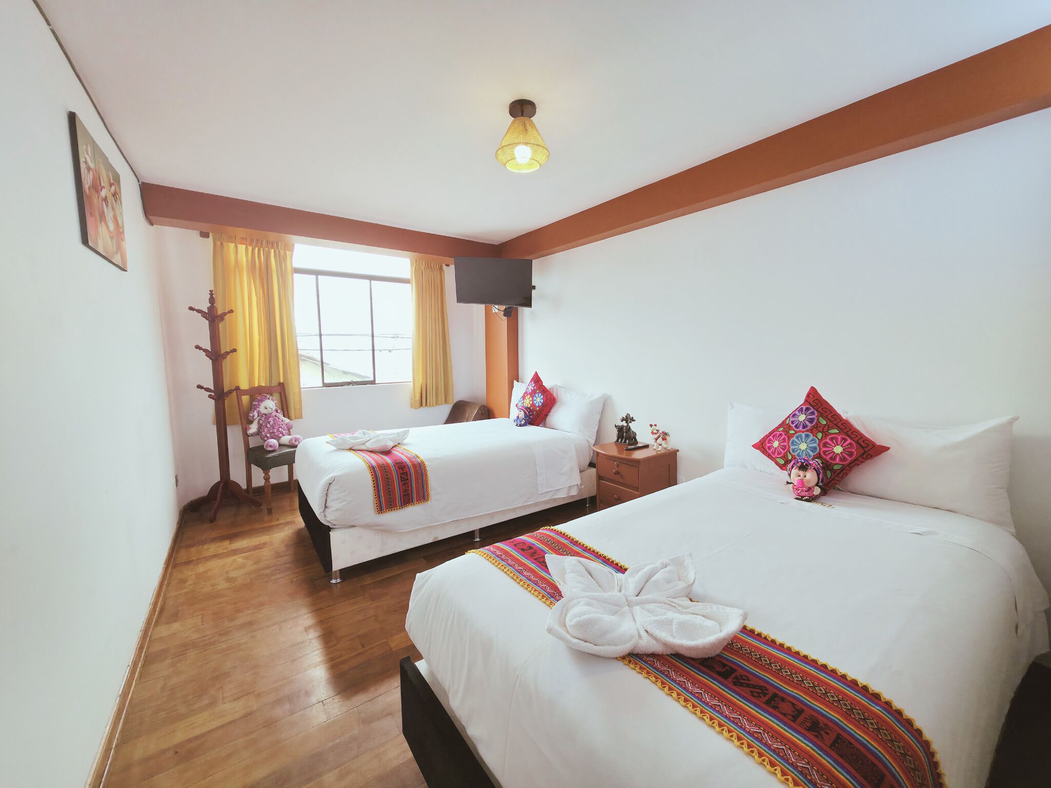 Une chambre d’hôtel avec deux lits, une télévision, un porte-manteau et une fenêtre avec des rideaux.