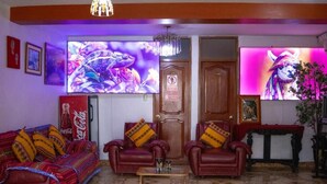 A living room with a sofa, two armchairs, a coffee table, and a television displaying a colorful image. - Mirador All Sur Cusco (Cusco)