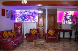Un salón con sofá, dos sillones, una mesa de centro y un televisor mostrando una imagen colorida.