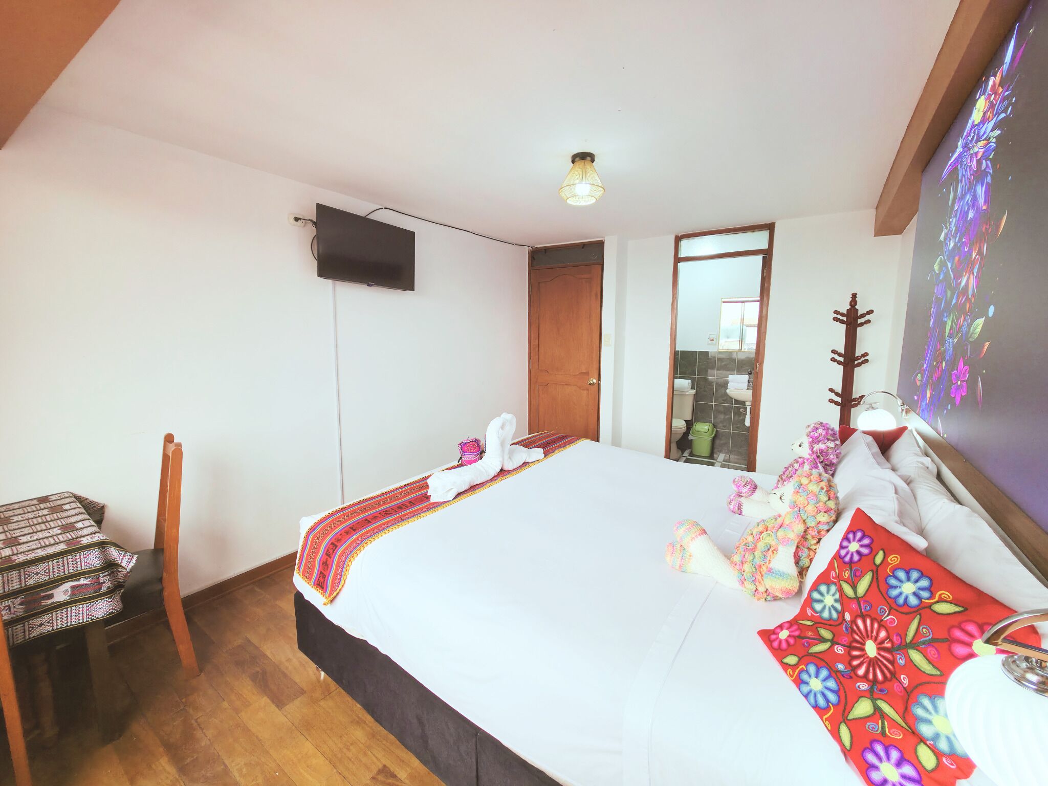 A hotel room with a bed, a desk, a television, and a bathroom visible through an open door.