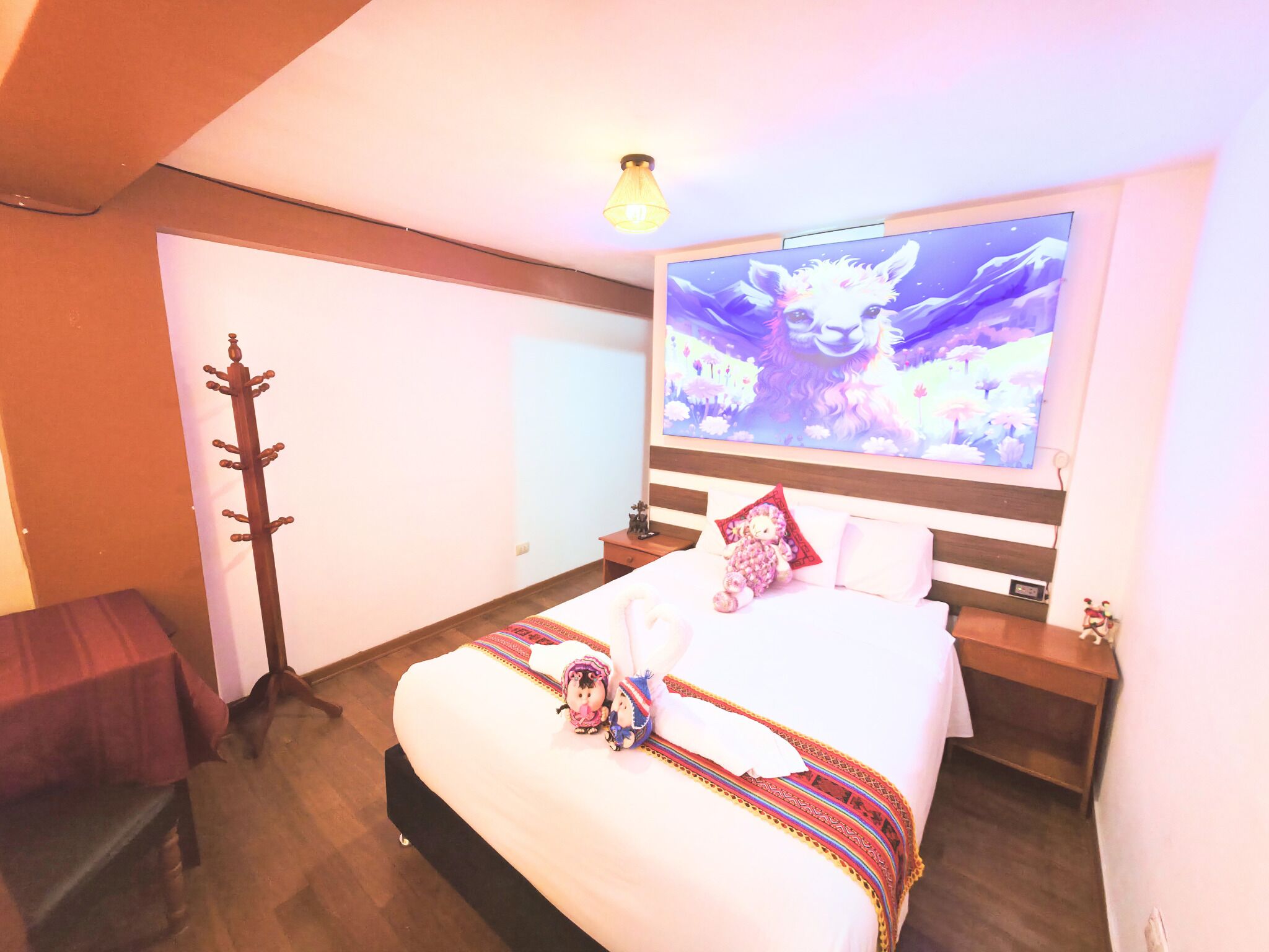 A hotel room with a bed, a wall-mounted TV, a wooden coat rack, and a small table.