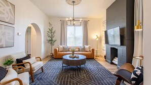 Een woonkamer met een bank, stoelen, een salontafel, een open haard en een televisie.