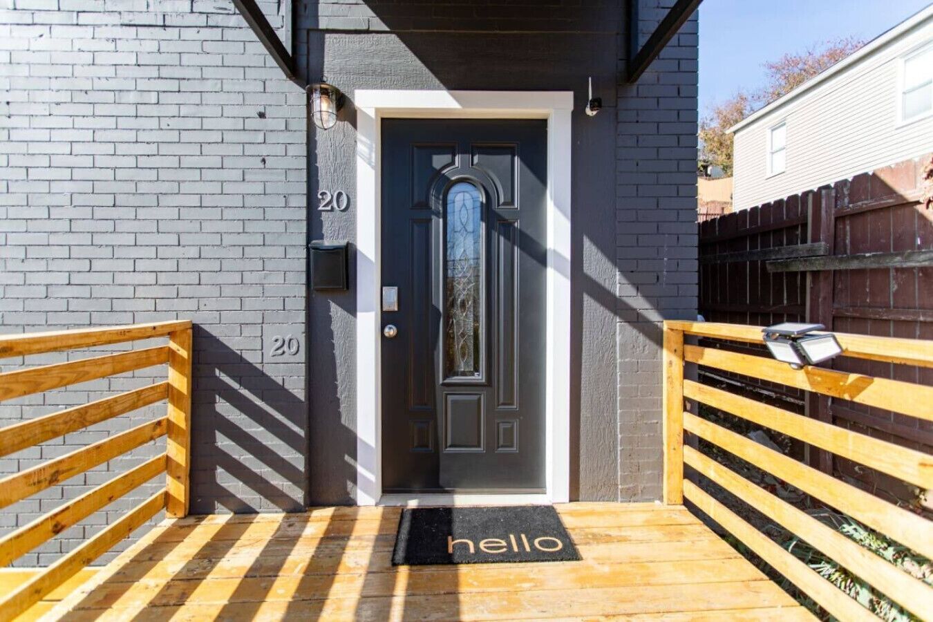 A black door with a glass panel, a wooden bench, and a 'hello' mat at the entrance.