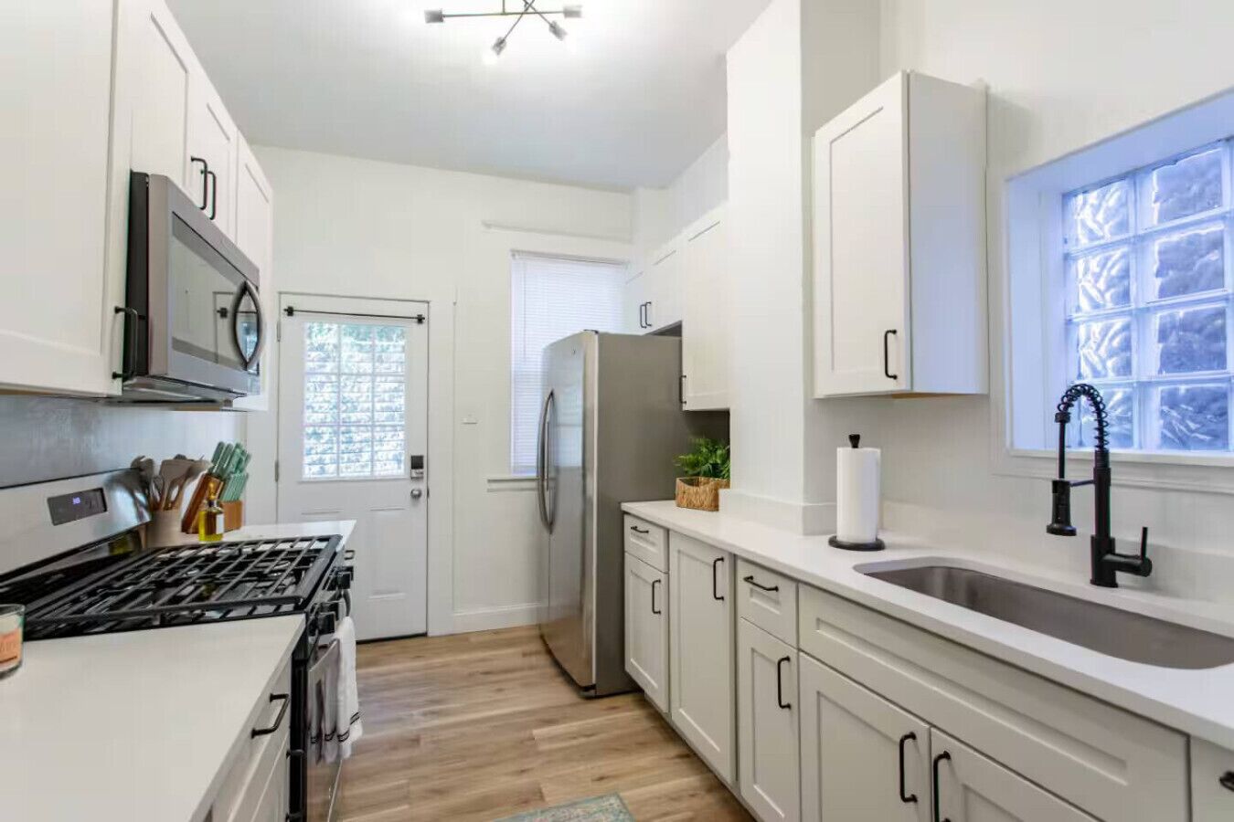 A modern kitchen with white cabinetry, a stainless steel refrigerator, a black faucet, and a window with frosted glass.