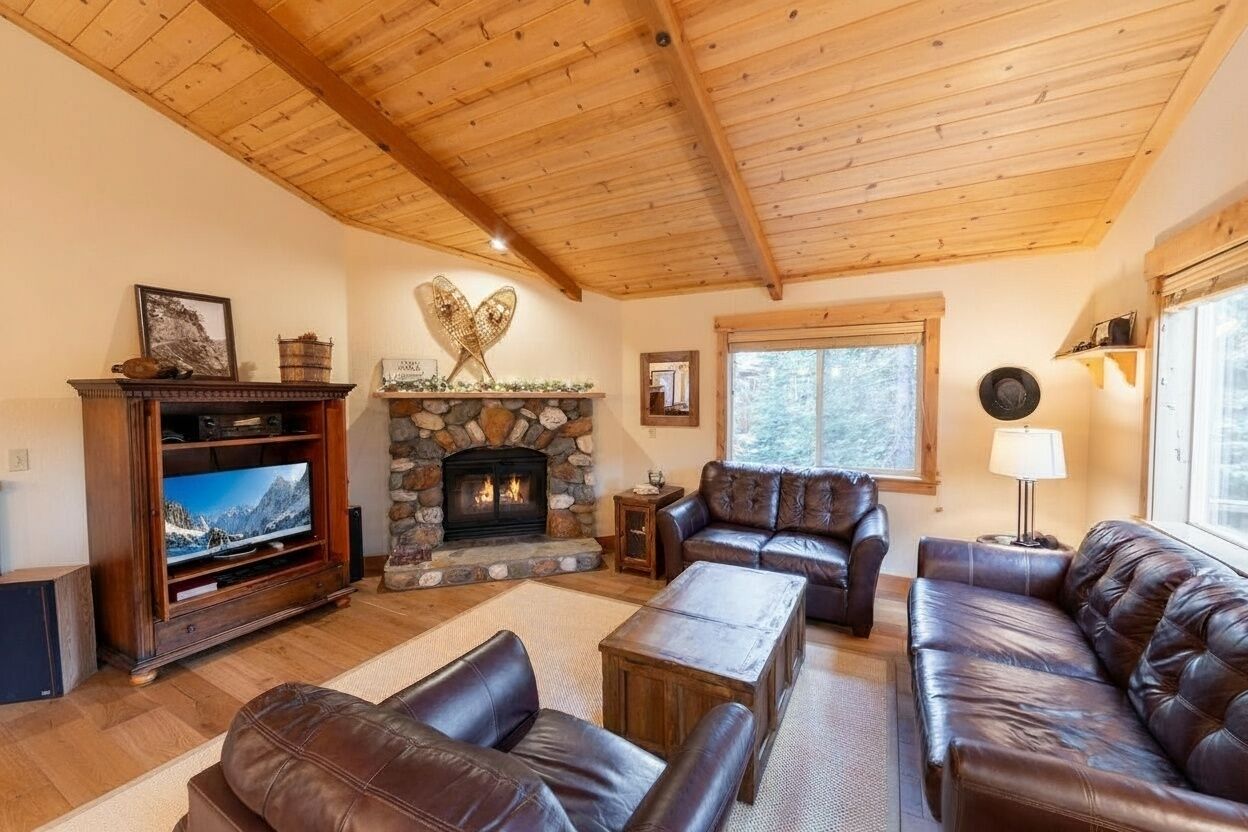 Ein gemütliches Wohnzimmer mit Kamin aus Stein, Ledersofas, einem Fernseher und einer Holzbalkendecke.