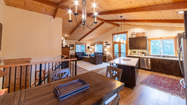 Een ruime keuken met houten kastjes, een eethoek met een houten tafel, en een woonruimte in loft-stijl met een bank en een kroonluchter.