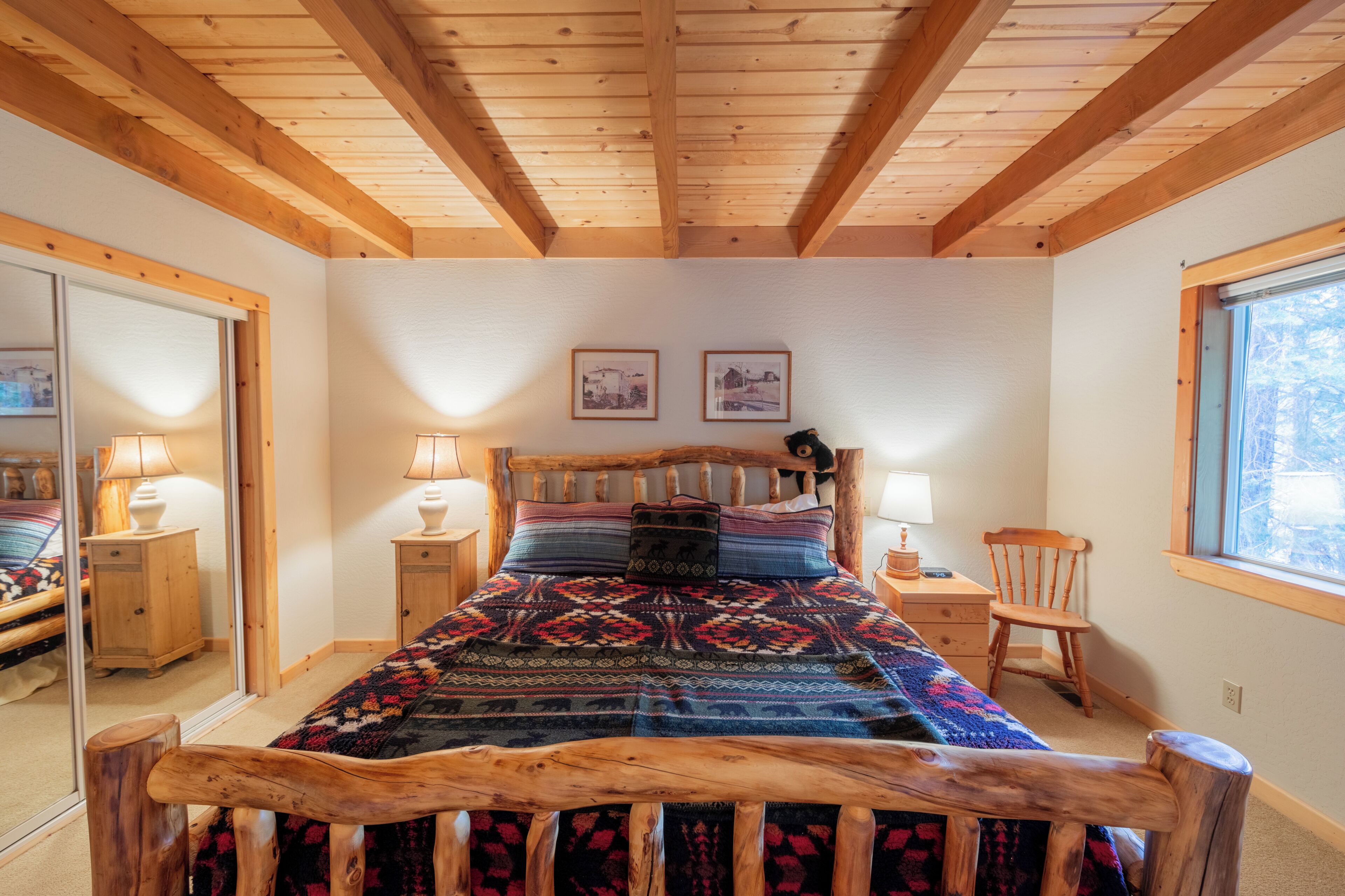 Quarto com estrutura de cama de madeira, um espelho grande e janela com vista.