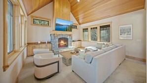 Un salon spacieux doté d’une cheminée en pierre, d’un plafond en bois et de grandes fenêtres.