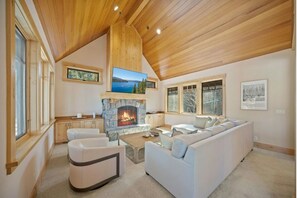 Ein geräumiges Wohnzimmer mit Kamin aus Stein, Holzboden und großen Fenstern.