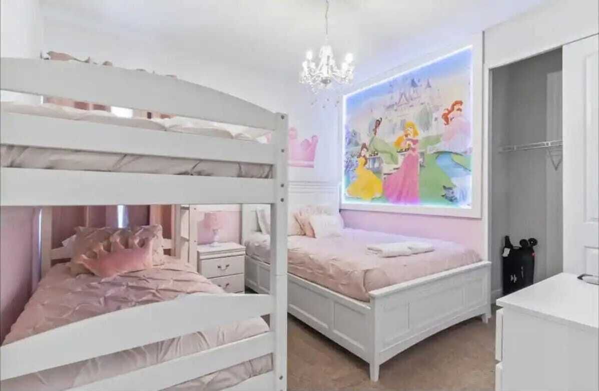 A bedroom with bunk beds, a chandelier, a wall mural, and a white dresser.