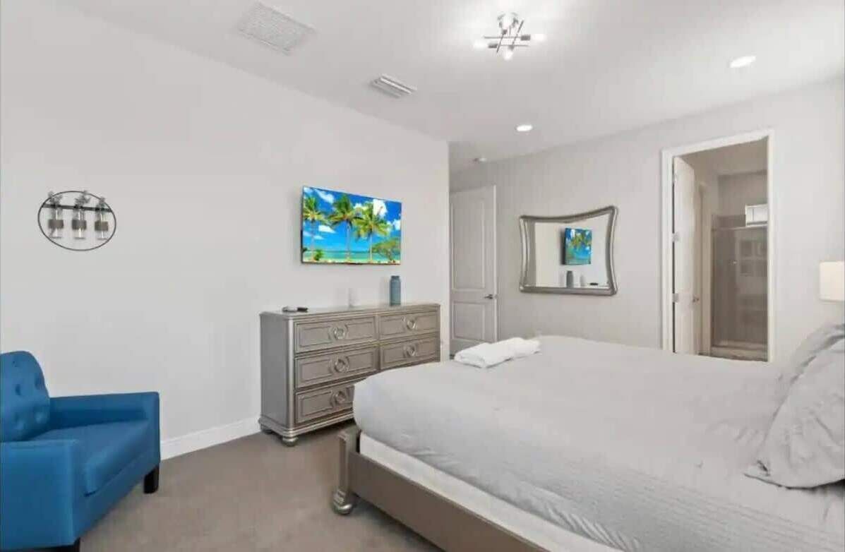A bedroom with a bed, a dresser, a blue chair, and a painting on the wall.