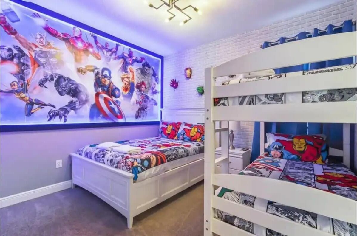 Quarto de criança com beliches, um mural na parede e um lustre.