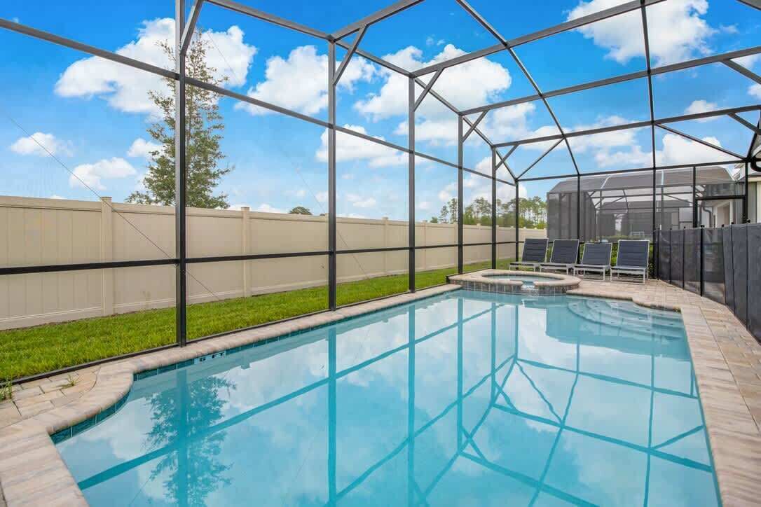 A clear blue pool with a metal roof structure, surrounded by a grassy area and a fence.