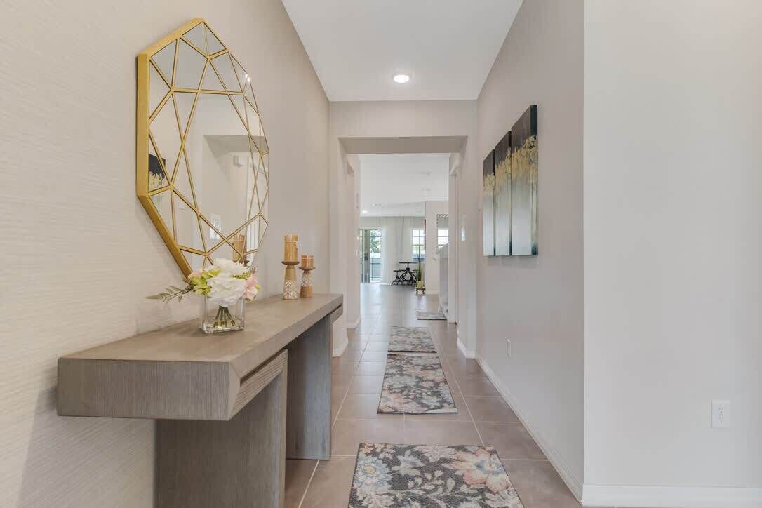 A hallway with a geometric mirror, a console table with flowers, and a rug.