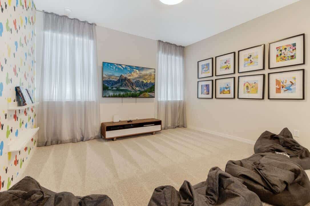 Ein Zimmer mit einem großen Flachbildfernseher, einem Berglandschaftsbild, einer Reihe gerahmter Bilder an der Wand und einem weißen Regal mit verschiedenen Gegenständen.