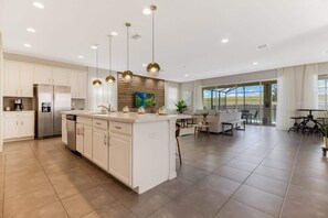 A modern kitchen with white cabinets, a central island, and pendant lighting. - Upscale 9BR Stay With Pool and Themed Rooms (Kissimmee)