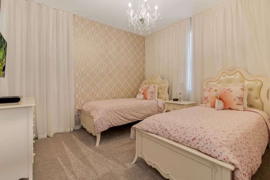 A bedroom with two beds, a chandelier, and a patterned wall.