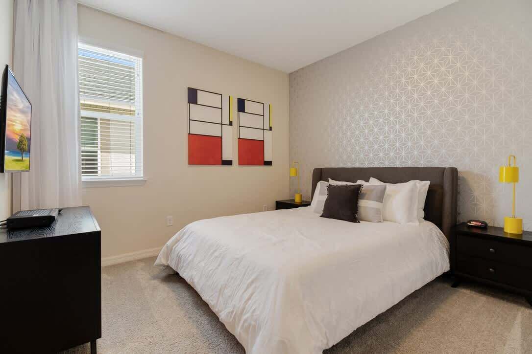 A bedroom with a bed, a desk, a TV, and artwork on the wall.