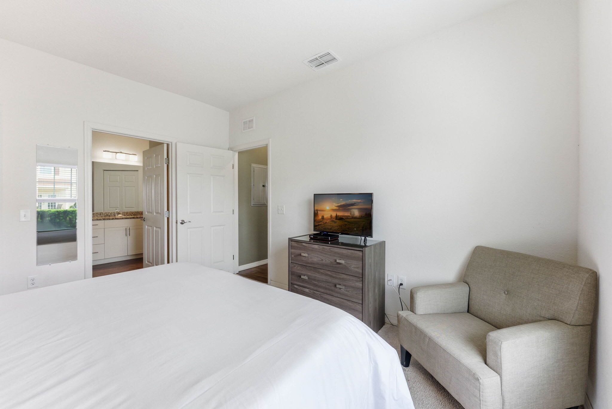 A bedroom with a bed, a dresser, a television, and a sofa.