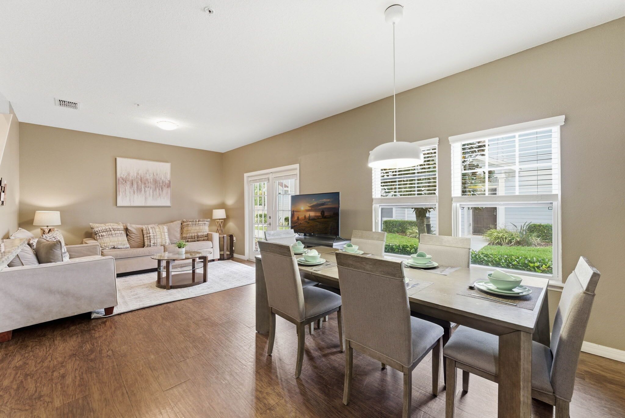A living room with a sofa, coffee table, dining table with chairs, a TV, and a window with blinds.