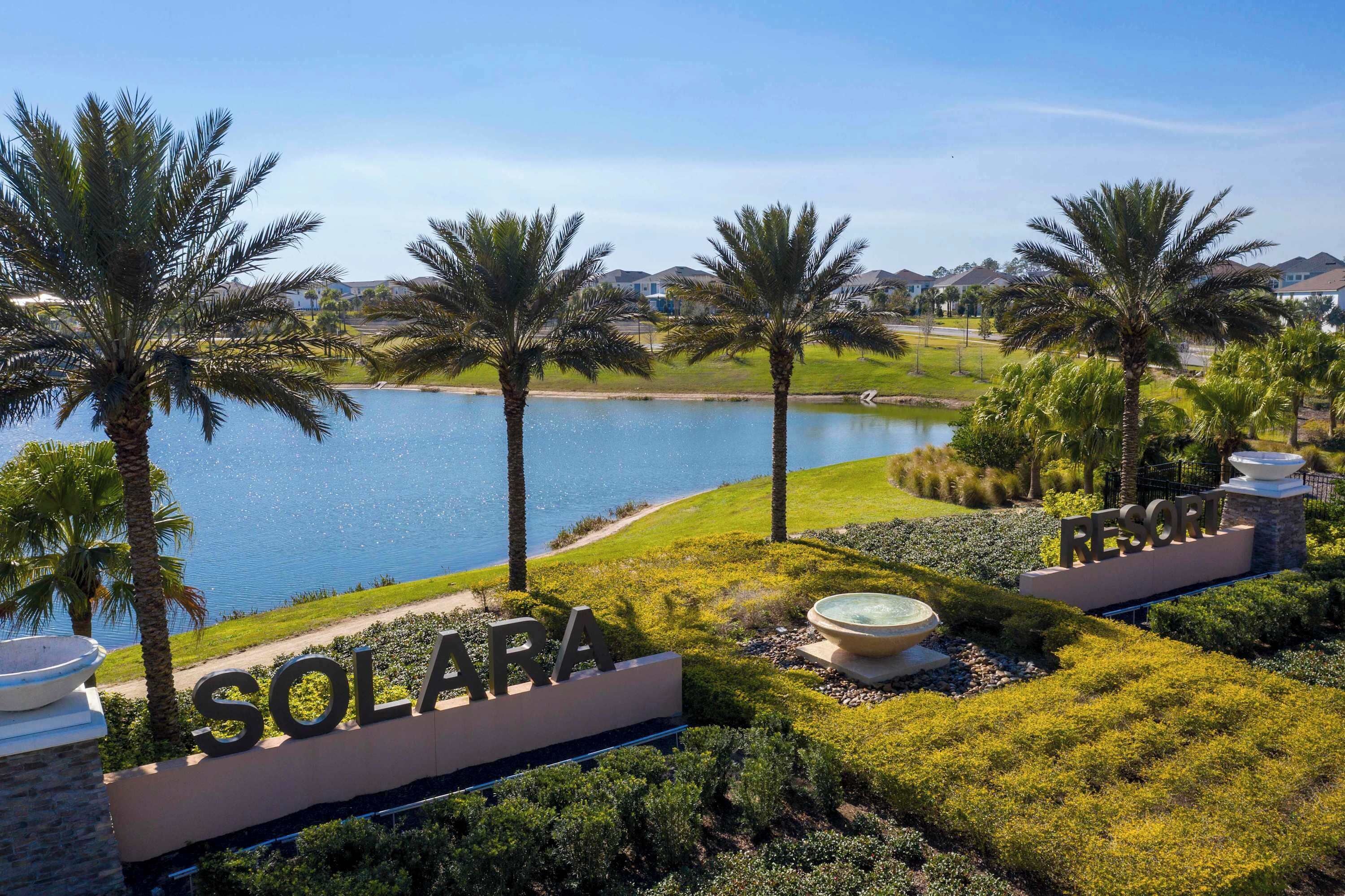 A resort named Solara with a view of a lake, palm trees, and a well-maintained lawn.