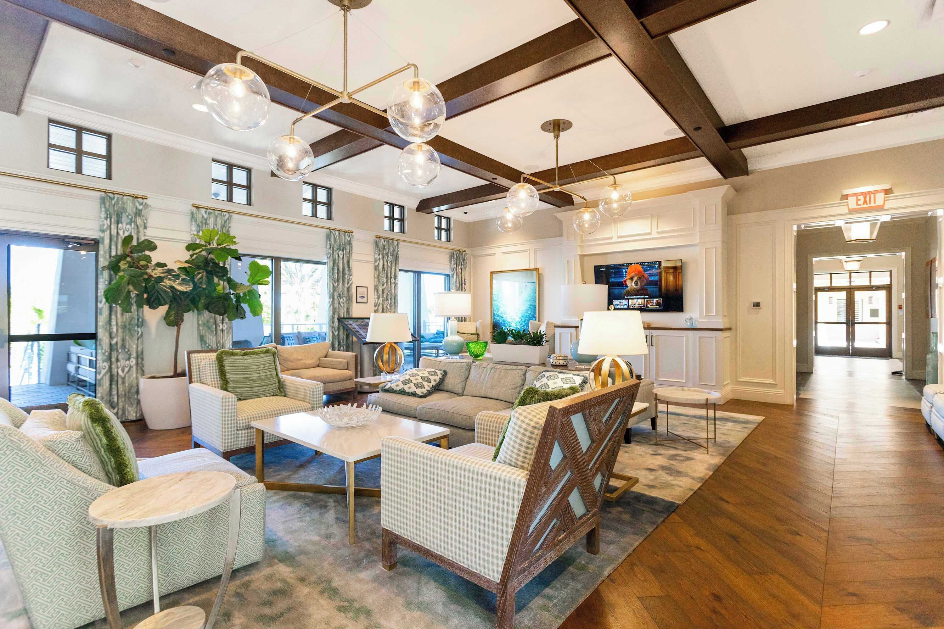 A spacious living area with a high ceiling, wooden beams, and a large window. There are multiple seating options including a sofa, armchairs, and a coffee table.