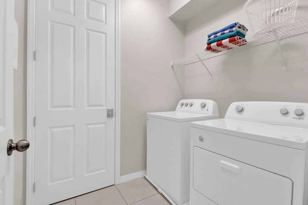 A laundry room with a white door, a stacked washer and dryer, and a shelf with folded towels.