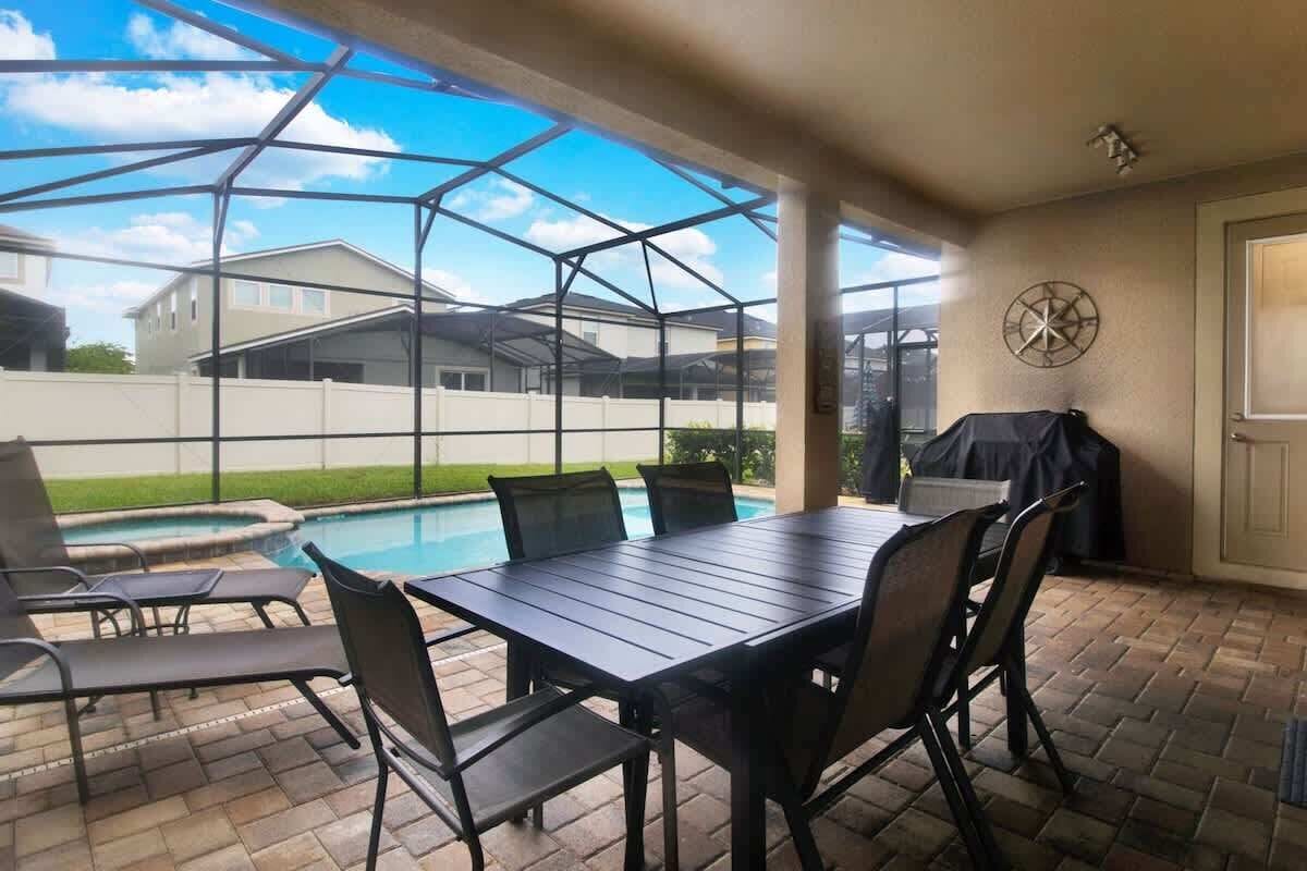 An outdoor patio with a table and chairs, a barbecue grill, and a pool.