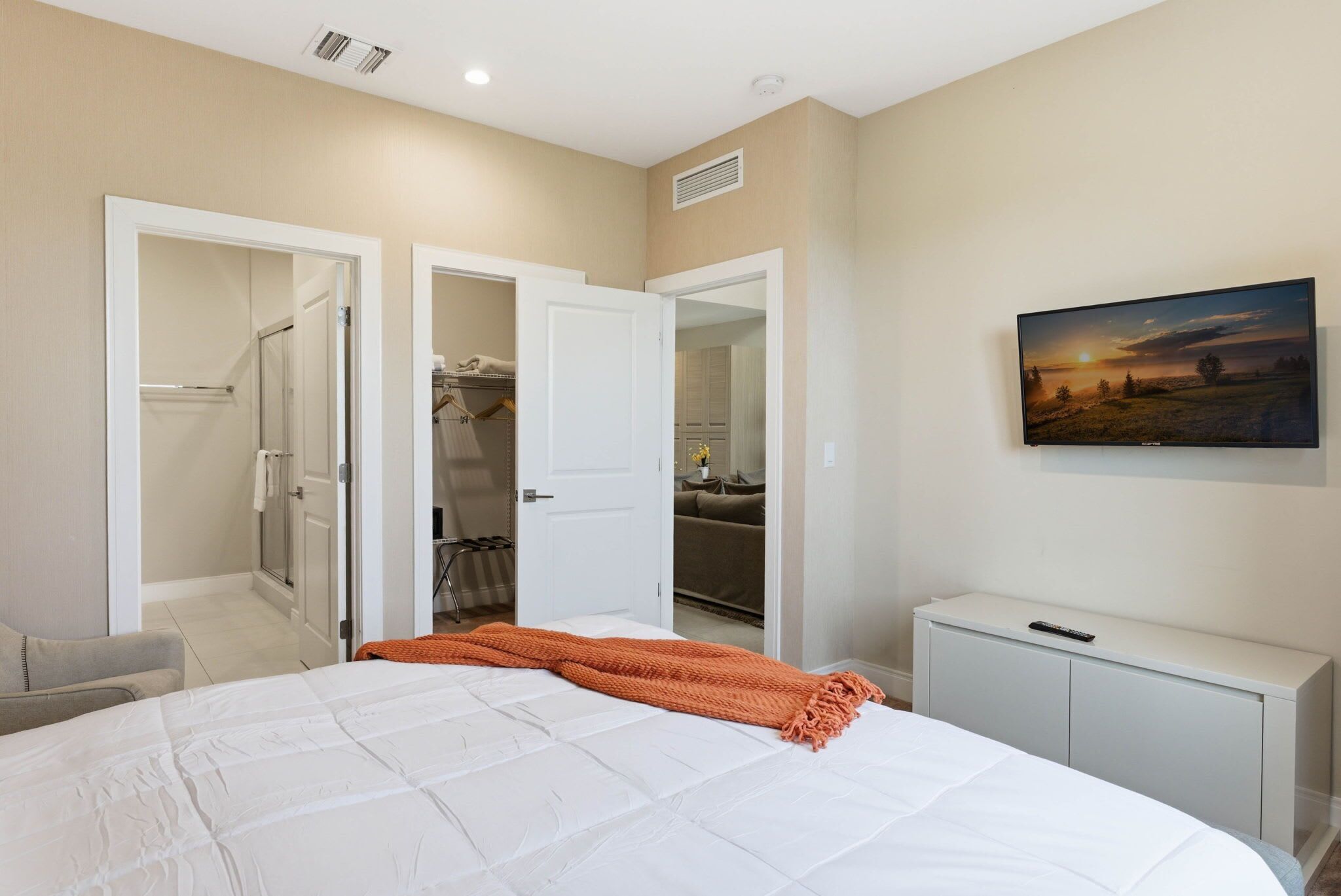 A bedroom with a bed, a wardrobe, a television, and a painting on the wall.
