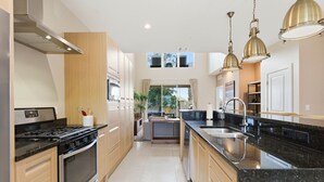 A modern kitchen with stainless steel appliances, wooden cabinets, a black granite countertop, and pendant lighting. - Magic Village 4br, Spacious and Stylish (Kissimmee)