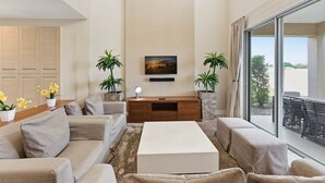 A modern living room with a sofa set, a coffee table, a TV mounted on the wall, and two potted plants. - Magic Village 4br, Spacious and Stylish (Kissimmee)