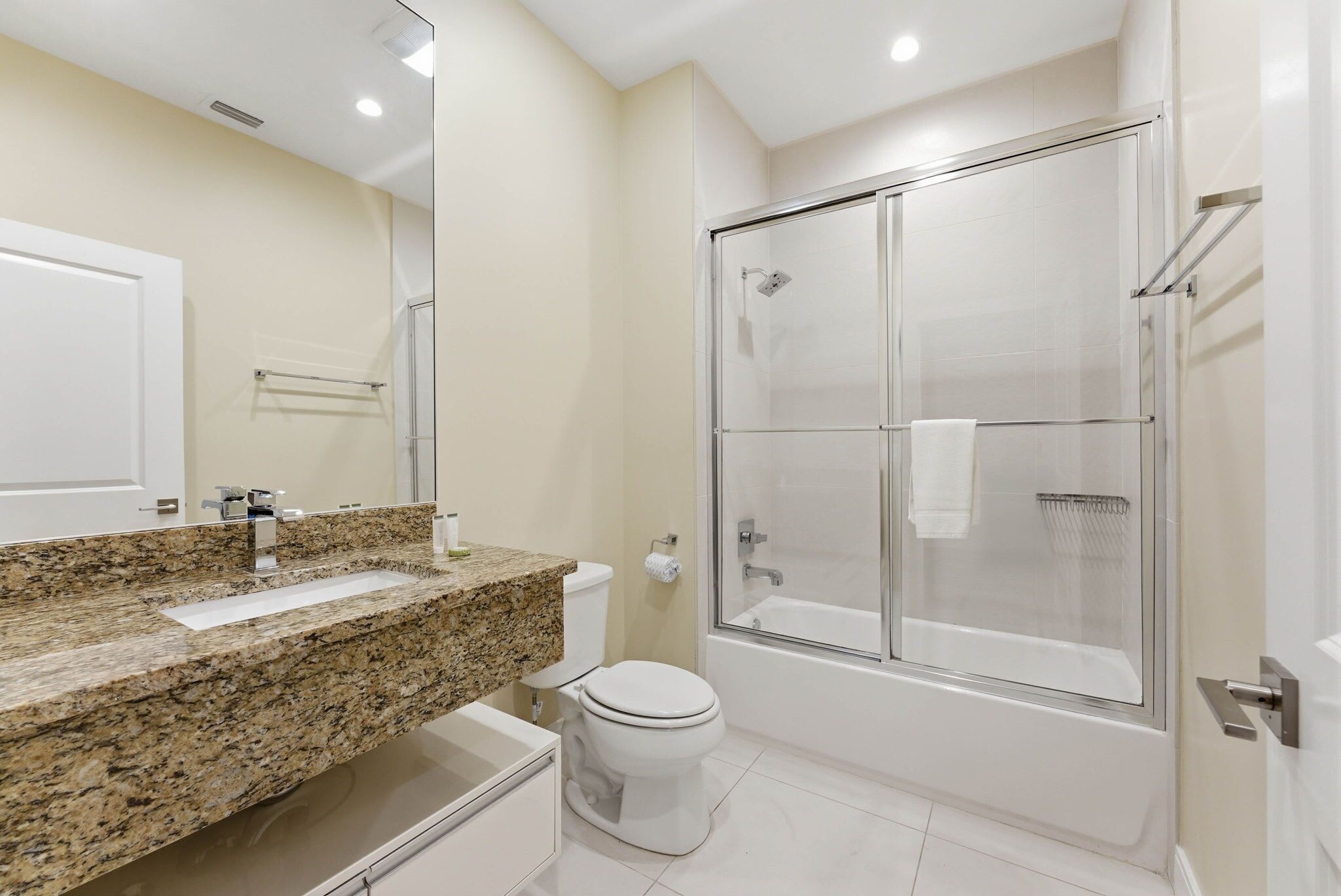 A bathroom with a granite countertop, a toilet, a glass-enclosed shower, and a white door.