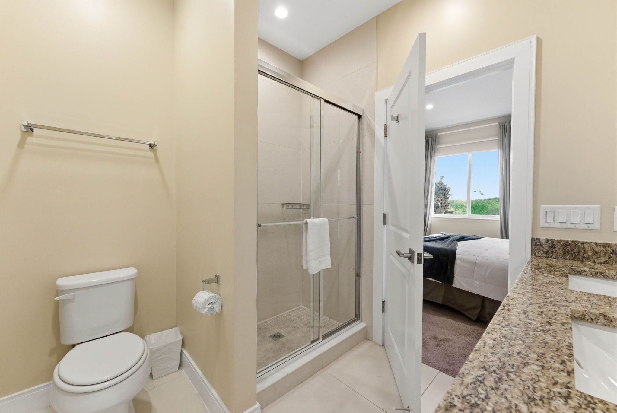 Een badkamer met toilet en douche, en een bed in de aangrenzende kamer.